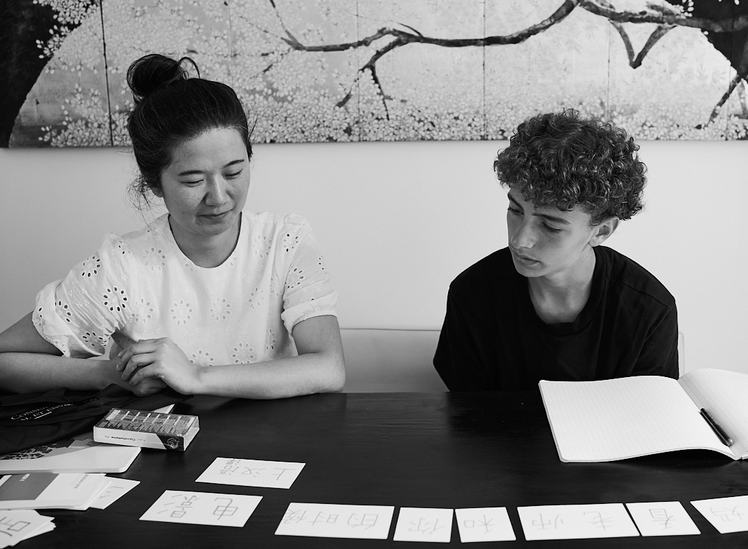 Min Luo accompagne un élève dans un exercice de lecture et de caractères chinois